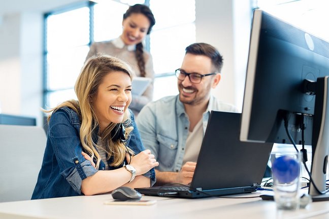 Drei Büromitarbeiter lachend bei der Arbeit am Computer