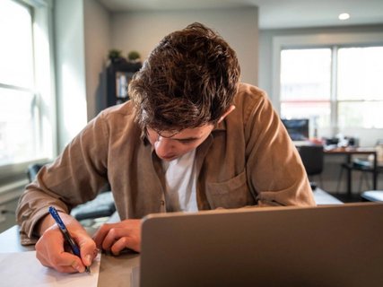 Junger Mann am Schreibtisch vor einem Laptop der ein Papier unterzeichnet