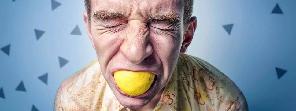 Mann beißt in eine Zitrone und verzieht sein Gesicht